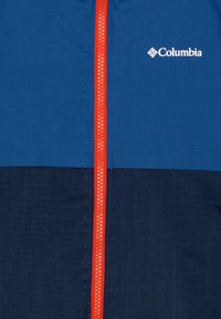 Blaue Jacke mit einem blau und marinefarbenen Blockdesign, ausgestattet mit einem auffälligen roten Reißverschluss und einem Columbia-Logo auf der oberen linken Seite.