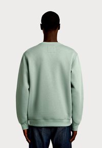 Miętowa zielona bluza z okrągłym dekoltem i ściągaczami na rękawach. Na plecach znajduje się kwadratowa naszywka z tkaniny. Miękka w dotyku i o luźnym kroju.