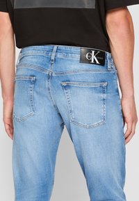 Vaaleansininen farkku, jossa on viisi taskua, suora leikkaus ja musta Calvin Klein Jeans -logoplässi vyötäröllä.