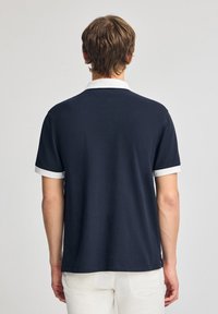 Marineblaues Poloshirt mit weißem Kragen und Ärmelabschlüssen. Kurzarm, weiche Textur und gerade geschnittenes Design.