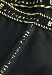 Zwarte stoffen onderbroek met een zachte textuur, voorzien van een elastische tailleband met "Ted Baker" in gouden letters en een contrasterend logo-detail.