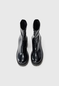 Bottines en cuir noir avec une texture lisse, un bout arrondi et une semelle épaisse. Le design présente un haut de tige avec un minimum de couture.
