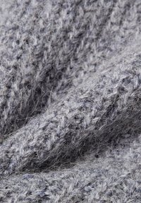 Grijze gebreide stof met een fluffy textuur. Het heeft losse steken en een zachte, warme uitstraling, waarmee de dikte en warmte van het garen wordt benadrukt.