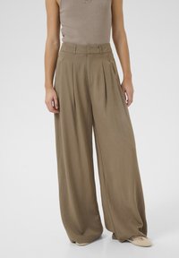 Wide-leg trousers in muted olive green fabric, featuring pleats, high waist, smooth texture, and a loose fit, paired with beige footwear.