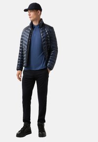 Námořnická pufovaná bunda s lesklou texturou, modré polo tričko, tmavé kalhoty a černé vysoké boty. Outfit má ležérní design.