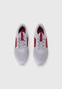 Zapatillas deportivas grises con acentos rojos, parte superior de malla para transpirabilidad y un logo negro en el costado. Incluye cordones y cuello acolchado.