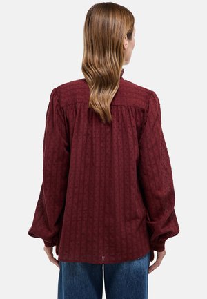 Chemise bordeaux à manches longues avec rayures verticales texturées et motifs à points, présentant une coupe décontractée et des manches retroussées, portée avec un jean bleu.