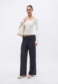 Krēmkrāsas garām piedurknēm krekls un tumši pelēkas plašas bikses, kombinētas ar gaiši bēšu krāsas plecu somu un mīkstām plakanām kurpēm. Gluda auduma, brīvs piegriezums.