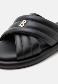 Sandale slide en cuir noir avec des brides croisées matelassées et une petite décoration lettre dorée "B" sur la bride supérieure.