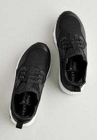 Black athletic shoes with mesh upper, padded collar, and white rubber sole. Features elastic laces and brand logo inside.
