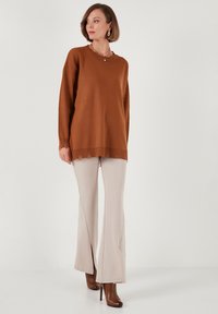 Maglione marrone a maglia con orlo a coste, abbinato a pantaloni beige chiaro a palazzo con spacchi. Modella che indossa stivali marroni con tacco.