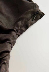 Schwarzer Satin-Stoff mit einem gerafften Design, das über einen diskreten Reißverschluss und eine glatte Textur verfügt, aus einer schrägen Ansicht gezeigt.