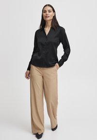 Schwarze Satin-Hemd mit langen Ärmeln und Knöpfen, kombiniert mit beigen weit geschnittenen Hosen und schwarzen Schuhen, mit glatter Textur und klassischem Design.