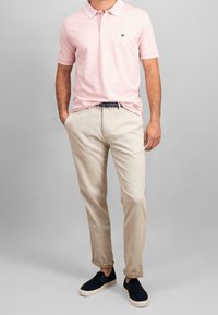 Vaaleanpunainen poolopaita, jossa on tummansininen logo, yhdistetty beigenvärisiin housuihin ja tummansiniset slip-on-kengät, joissa on vaalea pohja. Yksinkertainen muotoilu ja mukava istuvuus.