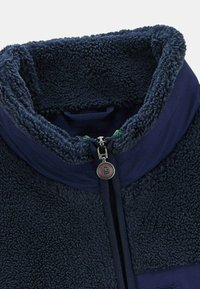 Veste en polaire marine avec un col haut, tissu texturé, fermeture éclair sur le devant et accents verts au niveau du col. Doublée pour la chaleur et le confort.