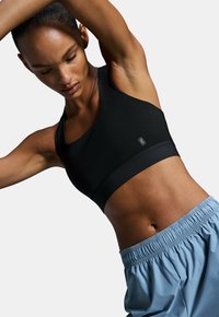 Soutien-gorge de sport noir avec des bretelles larges et une coupe ajustée, associé à un short bleu clair avec une taille élastique et une coupe ample.