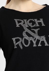 Felpa nera con scollatura ampia, decorata con strass che formano il testo "RICH & ROYAL." Tessuto morbido con vestibilità comoda.