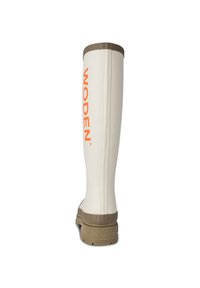 Botte en caoutchouc blanche avec une semelle marron, portant la mention "WODEN" imprimée en orange. Le design comprend des côtes verticales pr�ès du haut et une semelle texturée.