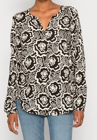 Blusa a maniche lunghe in bianco e nero con motivo floreale, scollo a V e dettagli con bottoni. Tessuto morbido con vestibilità ampia.