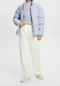 Lichtblauwe donsjas met een hoge kraag, gecombineerd met een grijze trui en witte wijde broekspijpen. Beige sneakers maken de outfit compleet.