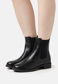 Zwarte enkellaarsjes van soepel leer, met elastische zijkanten en een lage blokhak. Eenvoudig ontwerp met een elegante silhoeët.