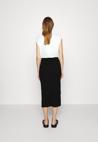 Bílý top s krátkým rukávem a zipem na zádech, spárovaný s přiléhavou černou midi sukní s jemným žebrováním. Celý outfit doplňují jednoduché černé ploché boty.