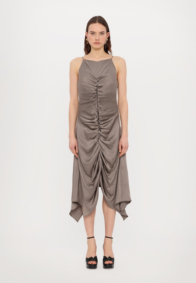 Gray satin dress with a gathered front design, creating draped texture. It has thin straps and an asymmetrical hem. Worn with black platform heels.