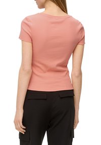 Korte mouwen, geribbeld, licht perzikkleurig topje met een ronde hals, gecombineerd met zwarte onderkleding met achterzakken met klep en taps toelopende benen.