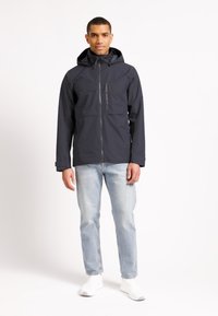 Laivaston vedenpitävä takki, jossa on etuvetoketju, kaksi rintataskua ja huppu. Yhdistetty vaaleansinihin farkkuihin ja valkoisiin lenkkareihin.