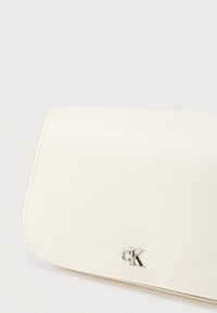 Κρέμ τσαντάκι χειρός κατασκευασμένο από λείο συνθετικό δέρμα. Διαθέτει κλείσιμο με καπάκι και ασημένιο λογότυπο ως διακοσμητικό στοιχείο. Καθαρές γραμμές με διακριτικές ραφές.