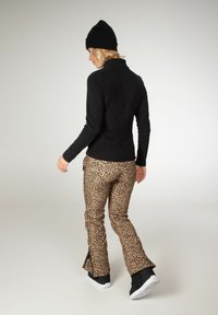 Čierny fleecový top a nohavice s leopardiou potlačou a zipsovými detailmi, doplnené čiernymi čižmami a čiernou čiapkou. Tkanina vyzerá mäkká a teplá.