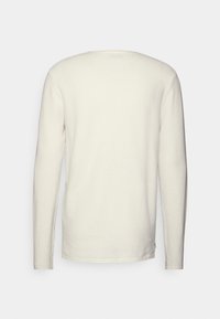 Sweter z długim rękawem w kremowym kolorze, o fakturze w stylu waflowym i luźnym kroju. Prosty design; bez zdobień i akcentów.