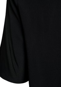 Tissu noir à texture lisse, présentant un design drapé et une manche ample, montrant des variations subtiles de lumière et d'ombre.