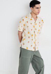 Short-sleeve shirt in light beige fabric featuring a fruit pattern with oranges and strawberries. Buttons down the front, relaxed fit.