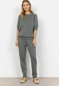 Completo loungewear grigio con top a maniche corte e maniche a sbuffo, abbinato a pantaloni con design affusolato. Tessuto morbido e confortevole.