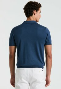 Marineblauwe katoenen polo met korte mouwen en een geribde kraag. Heeft een aansluitend ontwerp en een zachte textuur, gecombineerd met witte broek.