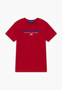 Červené bavlněné tričko s potiskem textu "POLO SPORT RALPH LAUREN" modrou a bílou barvou. Pod textem se nachází malá grafika americké vlajky.