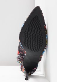 Chaussure à talon stiletto à bout pointu avec semelle noire et tige en tissu à motifs multicolores, vue par le dessous sur fond blanc.