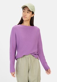 Lilla ribbet sweater med lange ærmer, rund hals og afslappet pasform, parret med en lysegrøn kasket og beige elastisk taljebukser.