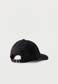 Μαύρο ρυθμιζόμενο καπέλο μπέιζμπολ που ακουμπάει στο πλάι, δείχνοντας το λουράκι με μεταλλική αγκράφα και τις οπές αερισμού στην κορυφή.