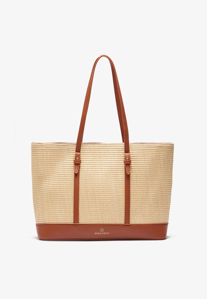 Woven straw tote bag with tan leather accents and dual shoulder straps. Features a solid base and subtle logo detailing on the front.