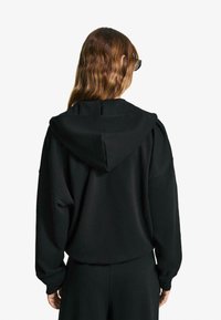 Black hooded sweatshirt made of soft fabric, featuring a relaxed fit and large hood, with dropped shoulders and ribbed cuffs.