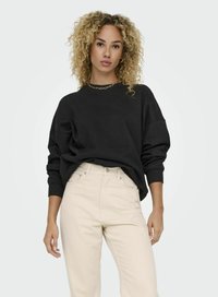 Svart oversized sweatshirt med rund halsringning och sänkta axlar, tillsammans med ljusbeige högmidjade jeans. Slät tygtextur, minimalistisk design.