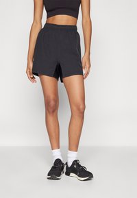 Svarta shorts med elastisk midja och avslappnad passform, med en subtil glans och sidofickor för rörlighet. Stylar med svarta sportskor och vita strumpor.