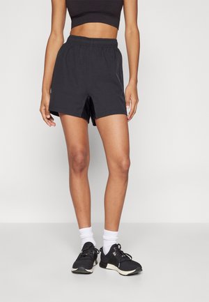 Sorte shorts med elastisk talje og afslappet pasform, der har en diskret glans og sidespalter for bedre bevægelsesfrihed. Stylet med sorte sportssko og hvide sokker.