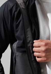 Black zip-up jacket with a smooth, matte fabric. Features a front zipper and a contrasting inner lining, worn over a white shirt.