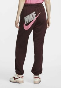 Maroon sweatpants with a large white and pink Nike logo on the back; features elastic waistband and cuffs, made of soft fabric.