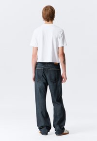 T-shirt branca curta com mangas curtas combinada com jeans azul escuro de corte amplo. Os jeans possuem cinco bolsos e costuras em contraste.