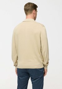 Pulover din tricot bej cu guler clasic, mâneci lungi și tiv ribbit. Textură netedă, fason mulat și fără modele sau accente vizibile.