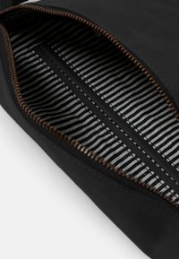 Schwarze Lederbörse mit einem gestreiften Stofffutter. Verfügt über einen braunen Reißverschluss und eine glatte Textur. Das Innere beinhaltet eine Einschubtasche.